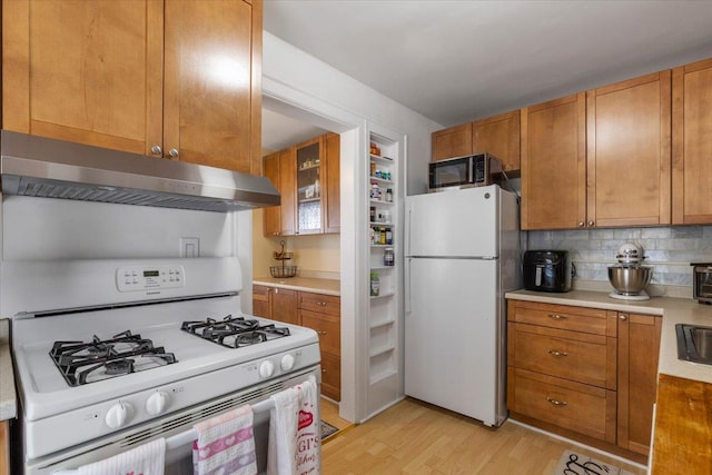 kitchen featuring decorative backsplash, white appliances, light wood-type flooring, light countertops, and under cabinet range hood
