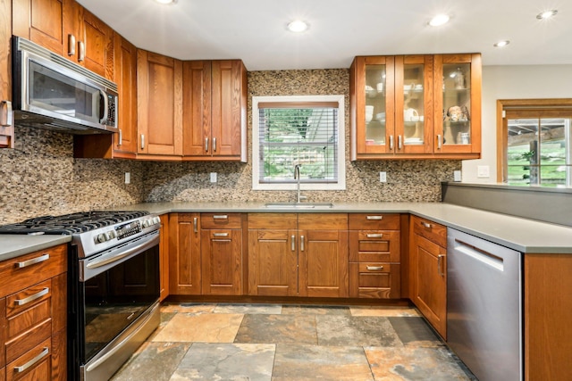 kitchen with brown cabinetry, stone finish flooring, tasteful backsplash, a sink, and stainless steel appliances