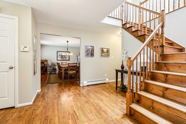 staircase featuring an inviting chandelier, baseboards, a baseboard heating unit, and wood finished floors