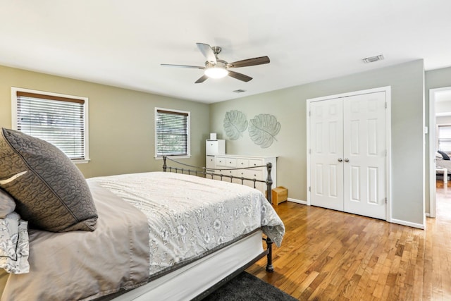 bedroom with a ceiling fan, visible vents, wood finished floors, baseboards, and a closet