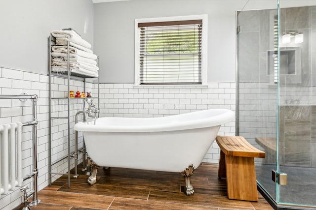 bathroom featuring wainscoting, radiator, tile walls, wood finished floors, and a stall shower