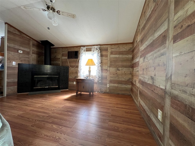 unfurnished living room featuring wood finished floors, wooden walls, visible vents, ceiling fan, and vaulted ceiling