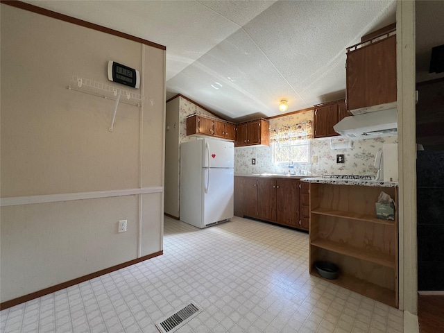 kitchen featuring freestanding refrigerator, visible vents, under cabinet range hood, light countertops, and vaulted ceiling