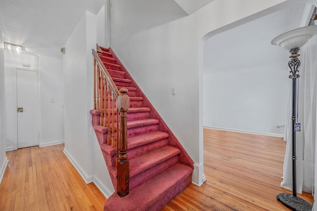 stairs featuring baseboards, arched walkways, and hardwood / wood-style floors