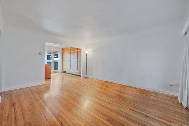unfurnished living room featuring arched walkways, ornamental molding, baseboards, and light wood-type flooring