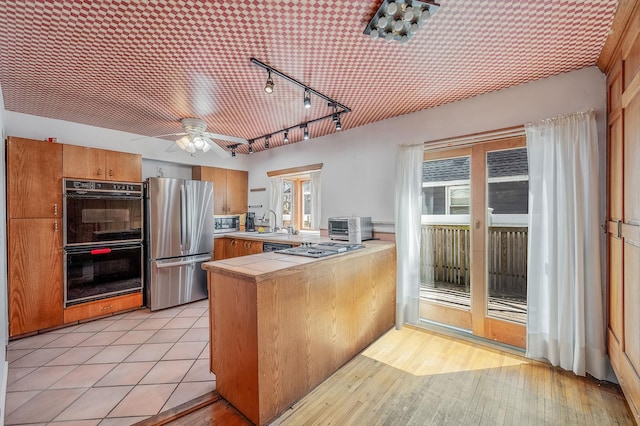 kitchen with a ceiling fan, appliances with stainless steel finishes, track lighting, a peninsula, and tile counters
