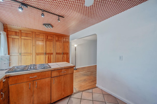 kitchen with stovetop with downdraft, arched walkways, rail lighting, baseboards, and tile counters