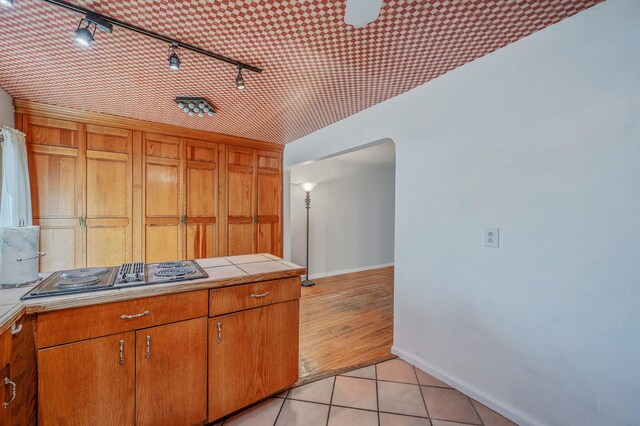 kitchen with stovetop with downdraft, arched walkways, rail lighting, baseboards, and tile counters