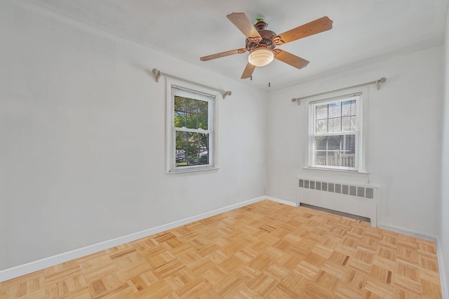 empty room with baseboards, radiator, ceiling fan, and a healthy amount of sunlight