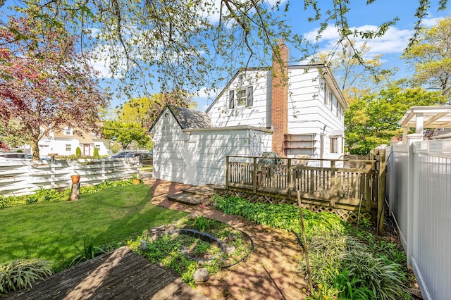 rear view of house featuring a yard, a deck, a chimney, and a fenced backyard