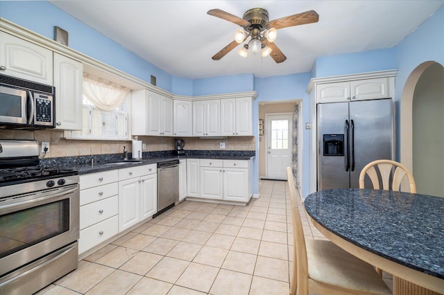 kitchen featuring decorative backsplash, a ceiling fan, arched walkways, stainless steel appliances, and light tile patterned flooring