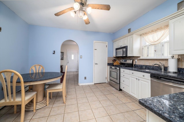 kitchen featuring ceiling fan, a sink, arched walkways, stainless steel appliances, and backsplash