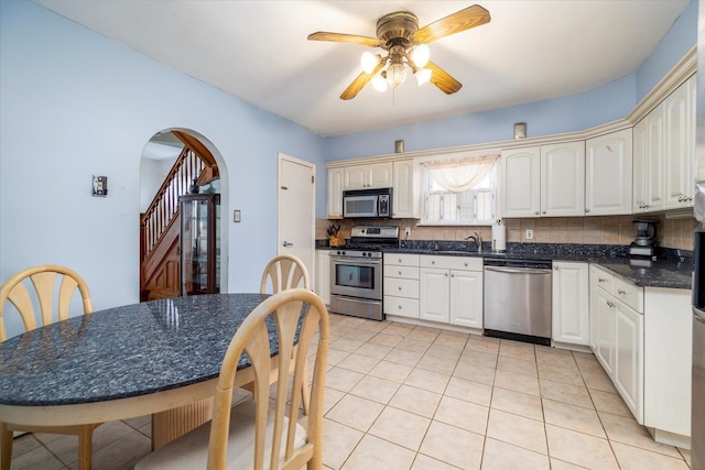 kitchen with dark countertops, ceiling fan, arched walkways, stainless steel appliances, and backsplash