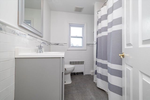 full bath with vanity, toilet, radiator, tile walls, and visible vents