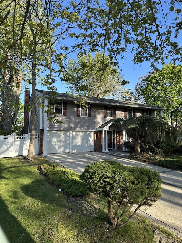 traditional home featuring an attached garage, a chimney, fence, and brick siding