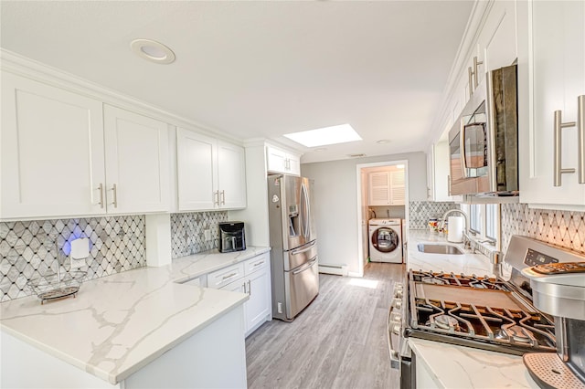 kitchen with white cabinets, appliances with stainless steel finishes, a sink, light wood-type flooring, and a baseboard heating unit