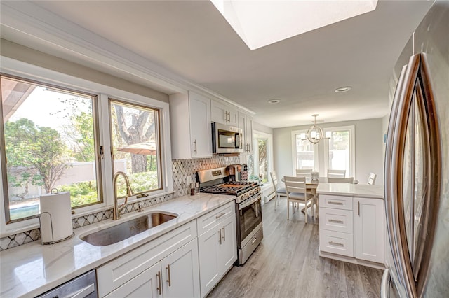 kitchen with backsplash, a sink, light stone counters, stainless steel appliances, and white cabinetry