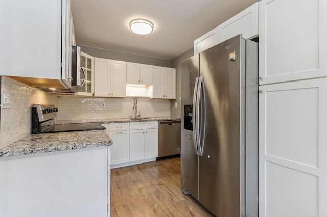 kitchen featuring backsplash, appliances with stainless steel finishes, a sink, white cabinets, and light wood-style flooring