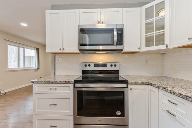 kitchen featuring decorative backsplash, wood finished floors, baseboards, white cabinetry, and stainless steel appliances