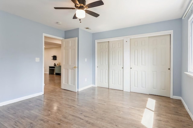 unfurnished bedroom with ceiling fan, visible vents, wood finished floors, baseboards, and multiple closets