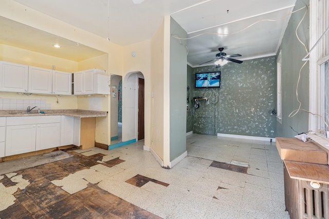 kitchen featuring ornamental molding, baseboards, ceiling fan, white cabinets, and arched walkways