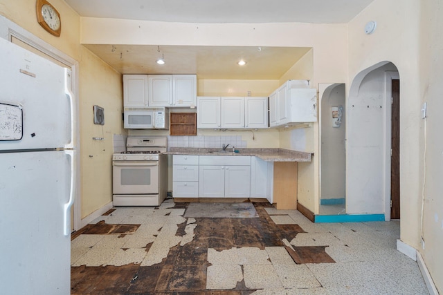 kitchen featuring a sink, white appliances, light countertops, white cabinetry, and baseboards