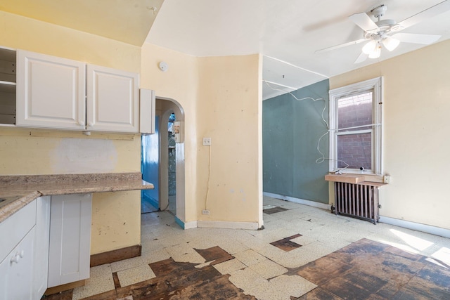 interior space with ceiling fan, arched walkways, radiator, baseboards, and light floors