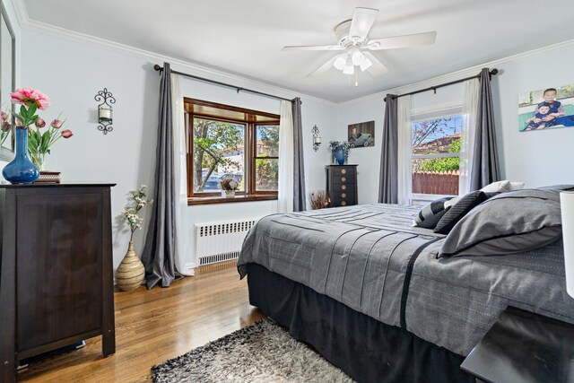 bedroom with wood finished floors, ornamental molding, radiator heating unit, and multiple windows
