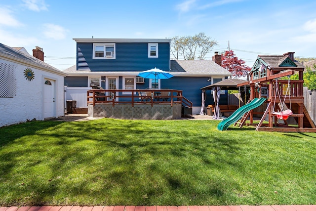 rear view of property with a lawn, a deck, fence, and a playground