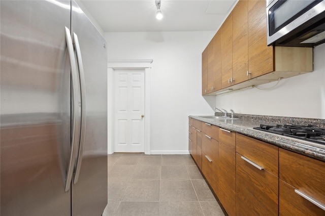 kitchen with dark countertops, a sink, brown cabinetry, stainless steel appliances, and baseboards