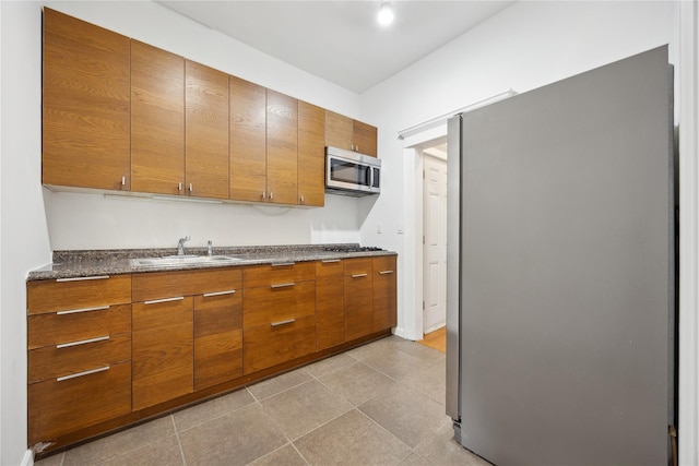 kitchen with stainless steel appliances, light tile patterned floors, brown cabinetry, and a sink