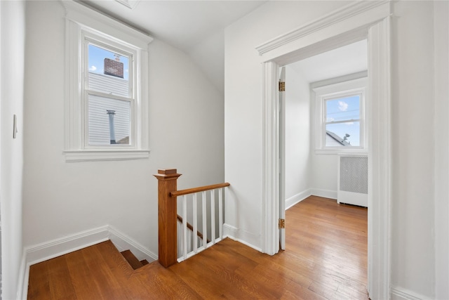 corridor featuring baseboards, wood finished floors, a wealth of natural light, and an upstairs landing