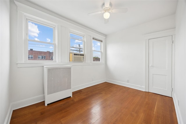 empty room with wood finished floors, baseboards, ceiling fan, and radiator heating unit