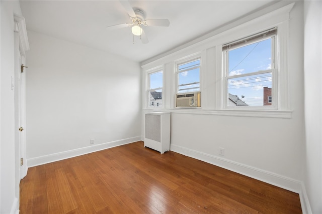 unfurnished room featuring baseboards, plenty of natural light, wood finished floors, and radiator heating unit