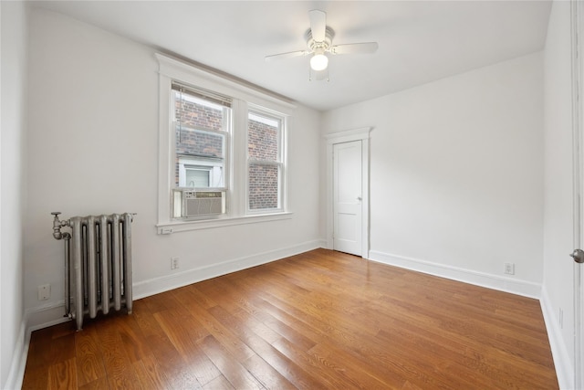 spare room featuring wood finished floors, baseboards, radiator heating unit, cooling unit, and a ceiling fan
