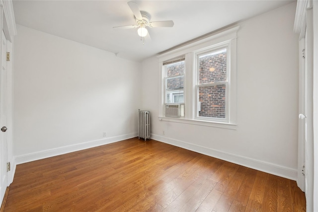 empty room featuring radiator, baseboards, a ceiling fan, and wood finished floors