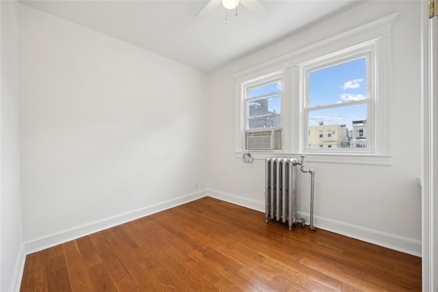 spare room featuring radiator heating unit, baseboards, a ceiling fan, and wood finished floors