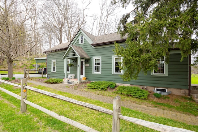bungalow with a shingled roof, a front lawn, and fence
