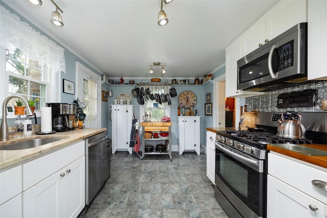 kitchen featuring stone finish floor, white cabinets, light stone counters, a sink, and appliances with stainless steel finishes