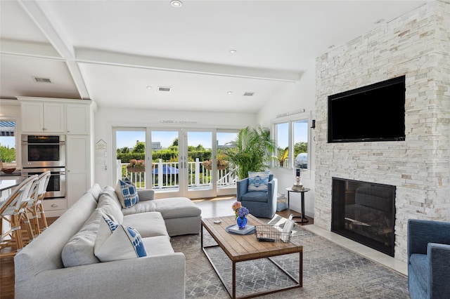 living room with lofted ceiling with beams, french doors, a stone fireplace, and visible vents