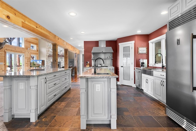 535 County Route 22, Middletown, NY 10940 - kitchen featuring stainless steel appliances, an island with sink, a sink, stone tile floors, and wall chimney exhaust hood