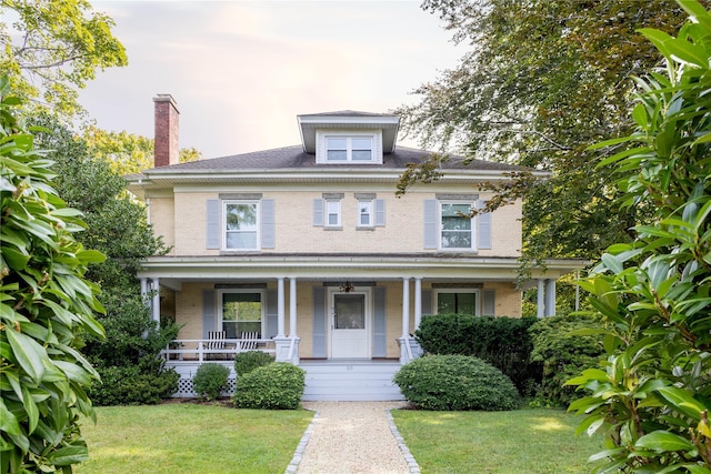 traditional style home with brick siding, a chimney, a front yard, and a porch