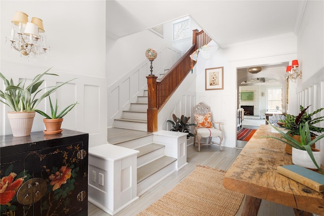 staircase with ornamental molding, wainscoting, a decorative wall, and a notable chandelier