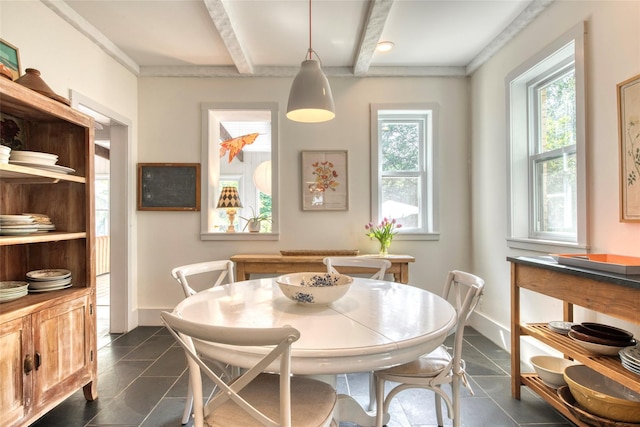 dining room with dark tile patterned floors, beam ceiling, and a healthy amount of sunlight