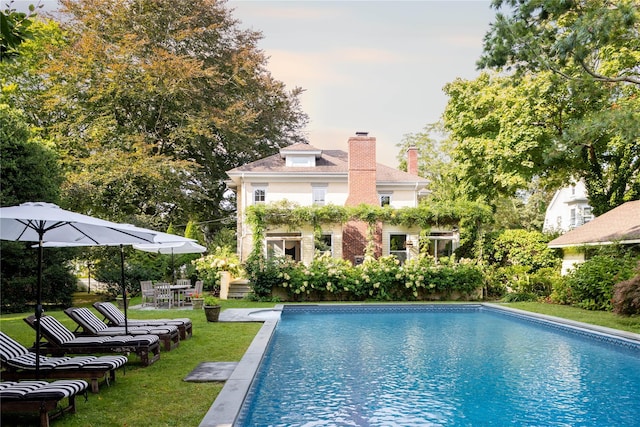 pool at dusk with a lawn, an outdoor pool, and a patio area