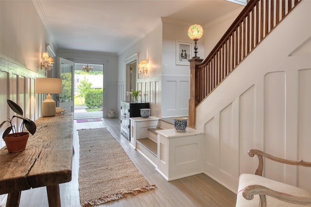 interior space featuring an inviting chandelier, wainscoting, a decorative wall, light wood-style flooring, and ornamental molding