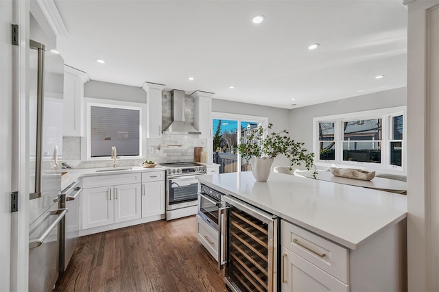kitchen with wall chimney range hood, white cabinets, a sink, beverage cooler, and stainless steel appliances