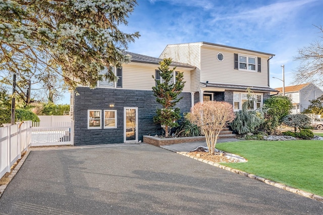 split level home with fence, driveway, a front lawn, and stone siding