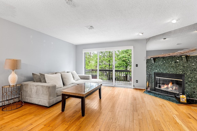 living area featuring visible vents, a textured ceiling, hardwood / wood-style flooring, and a tile fireplace