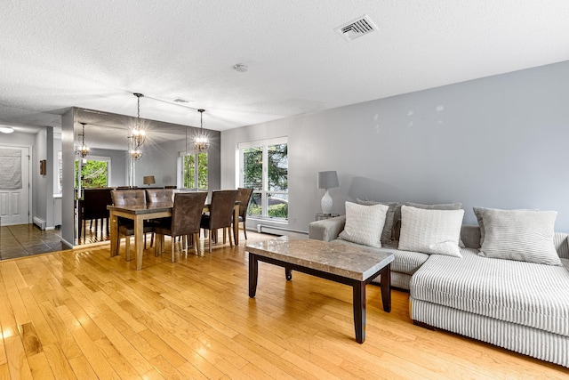 living area with a textured ceiling, visible vents, light wood-type flooring, a baseboard radiator, and a notable chandelier
